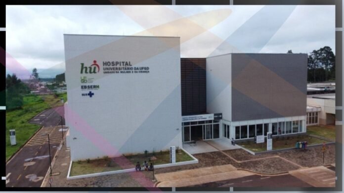 Aerial view of a modern university hospital building with white and gray walls, glass entrance, and a small group of people outside the front doors.