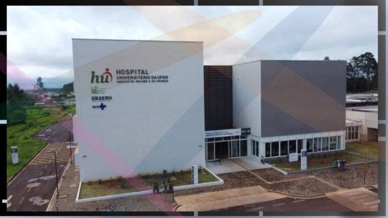 Aerial view of a modern university hospital building with white and gray walls, glass entrance, and a small group of people outside the front doors.