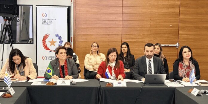 Panel of four delegates seated at a conference table with national flags (Uruguay, Brazil, Paraguay, Argentina) and nameplates, during a formal meeting; backdrop features the Ministerio de la Mujer Paraguay banner and a wooden wall.