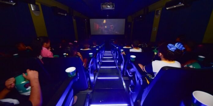 Dimly lit movie theater with blue-lit steps and audience watching a film on a large screen.