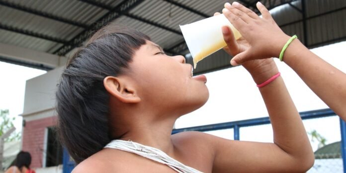 Girl tilts head back to drink juice from a disposable cup held by two hands outdoors.