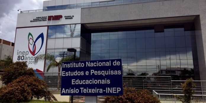 Glass-fronted INEP building with a large banner and a blue sign in the foreground reading 'Instituto Nacional de Estudos e Pesquisas Educacionais Anísio Teixeira-INEP'.