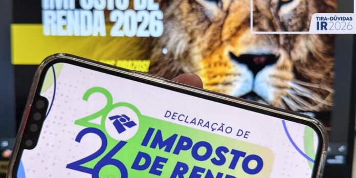 Smartphone screen showing a 2026 IR declaration graphic (Imposto de Renda 2026) with a lion poster in the background.
