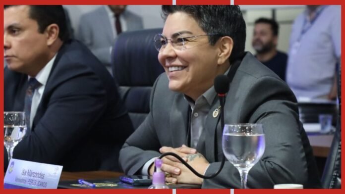 Smiling man in a gray suit sits at a conference table with a microphone in front of him.