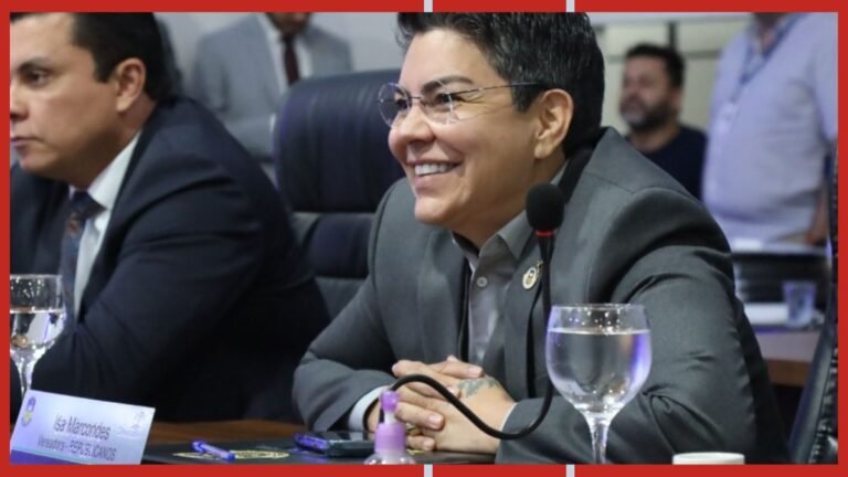 Smiling man in a gray suit sits at a conference table with a microphone in front of him.