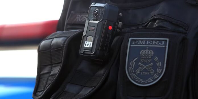 Close-up of a police vest with a mounted body-worn camera and a PMERJ patch on the chest area.