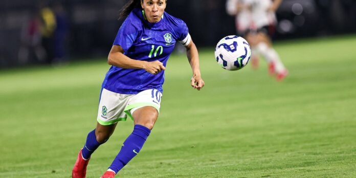 Brazilian female soccer player in blue jersey (number 10) running toward a ball on a green field during a match.