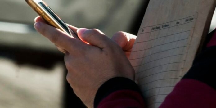 Close-up of hands holding a yellow pen and writing on a ruled clipboard with a form.