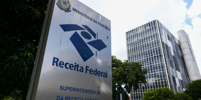 Sign for Receita Federal (Brazilian Federal Revenue) with government seal, in front of a modern office building.