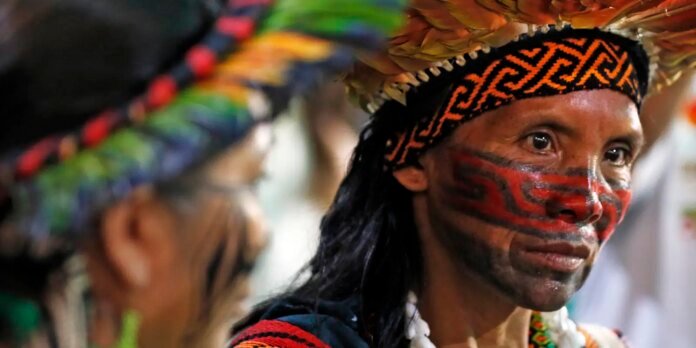 Close-up of a person with red and black tribal face paint, a patterned headband, and a straw hat at a festival.