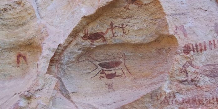 Ancient red rock art on a sandstone wall, showing a central crab figure with surrounding stick figures.