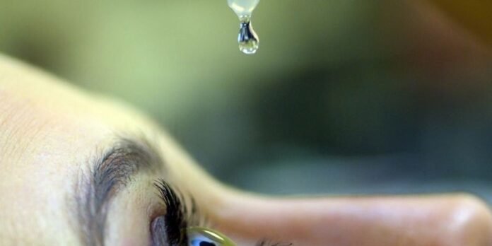 Close-up of an eye with a clear droplet about to fall from a dropper above the eye.