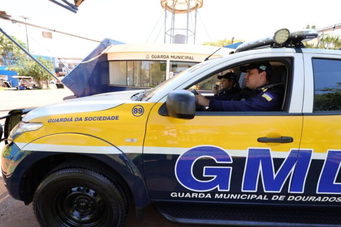 Yellow and blue Guarda Municipal patrol vehicle with two officers inside, parked by a Guarda Municipal building.