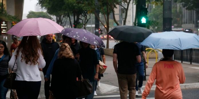 Crowd of pedestrians with colorful umbrellas crossing a city street in the rain, under a green pedestrian signal.