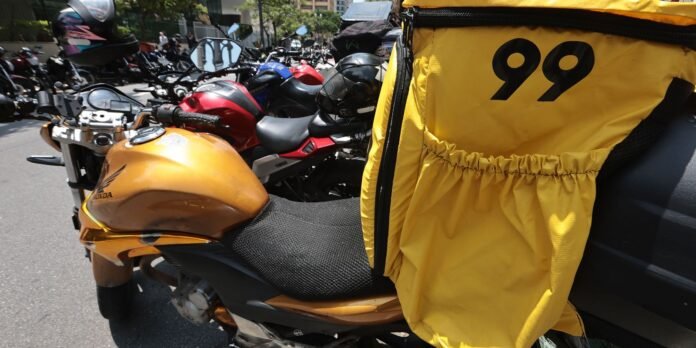 Orange Honda scooter with a large yellow courier bag labeled 99 attached to the rear, parked among many motorcycles.