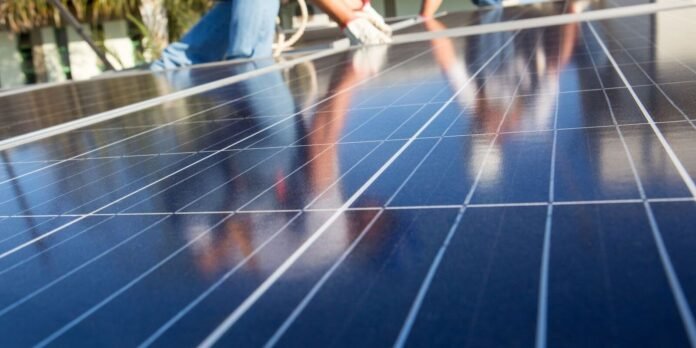 Close-up of glossy solar panels with workers in the background performing maintenance.