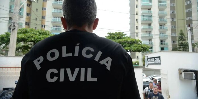 Person in a black jacket labeled 'POLICIA CIVIL' stands with their back to the camera outside a city police entrance, with buildings and pedestrians in the background.
