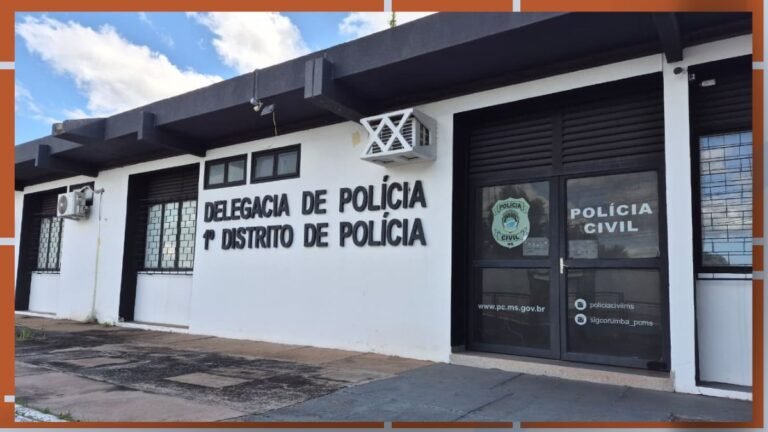 Frente de delegacia de polícia, prédio branco com letreiro 'DELEGACIA DE POLÍCIA 1º DISTRITO DE POLÍCIA' e porta de vidro com logotipo da Polícia Civil no lado direito da fachada interior.