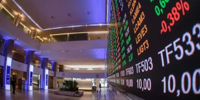 Interior of a modern stock exchange hall featuring a long black LED ticker wall with green, red, and white stock numbers; blue ambient lighting, tall pillars, and a few people in the background.