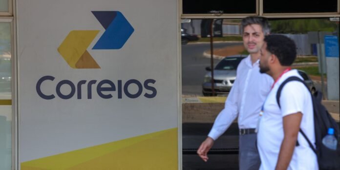 Exterior view of a Correios post office sign with two men walking by in the foreground.