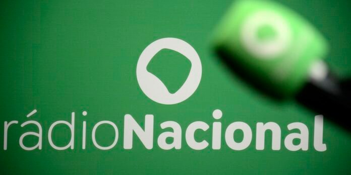Close-up of a green Radio Nacional sign with a white circular logo and a hand touching the right edge.