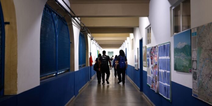 A group of people walking down a long indoor hallway with blue walls and posters on the right side.