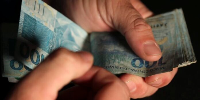 Close-up of hands counting blue 100 reais banknotes, showing Banco Central do Brasil text on the bills