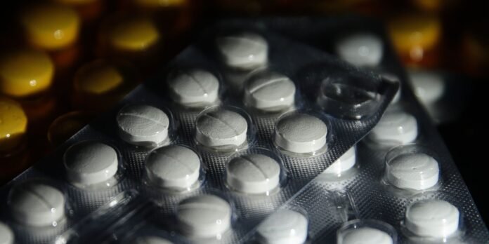 Close-up of blister packs with round white pills, angled with yellow pills blurred in the background.