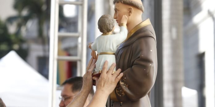 Statue of a robed man holding a child, as several people touch the statue during a public religious display