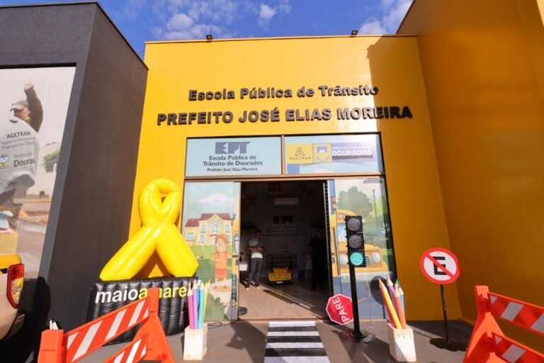 Entrance to Escola Pública de Trânsito Prefeito José Elias Moreira, yellow building with decorative traffic-themed props outside.