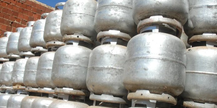 Stacks of silver metal propane gas tanks outdoors against a red brick wall on pallets.