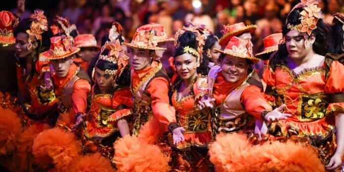 Group of dancers in bright orange and gold costumes performing a coordinated routine at a festival.