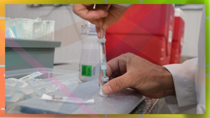 Healthcare worker drawing liquid from a vial into a syringe at a clinic counter