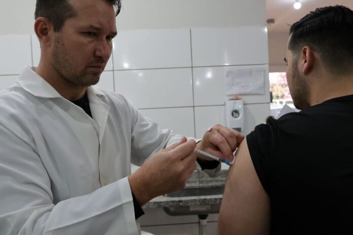 A clinician in a white coat administers a vaccination to a patient's upper arm with a syringe in a clinical setting