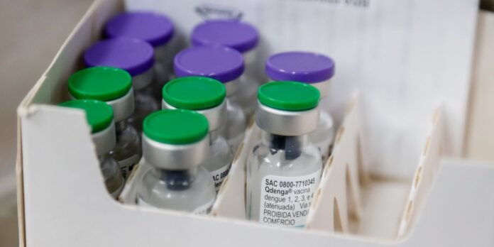 Vial bottles with green and purple caps arranged in a white cardboard vaccine tray in a clinical setting.
