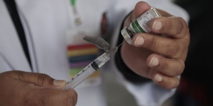 Healthcare professional drawing a vaccine from a vial into a syringe ready for administration.