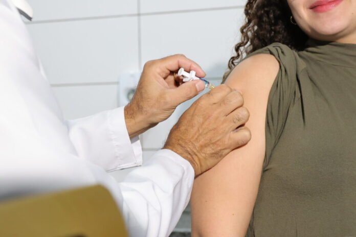 Healthcare professional administers a vaccine to a woman's upper arm in a clinical setting, close-up of the injection.