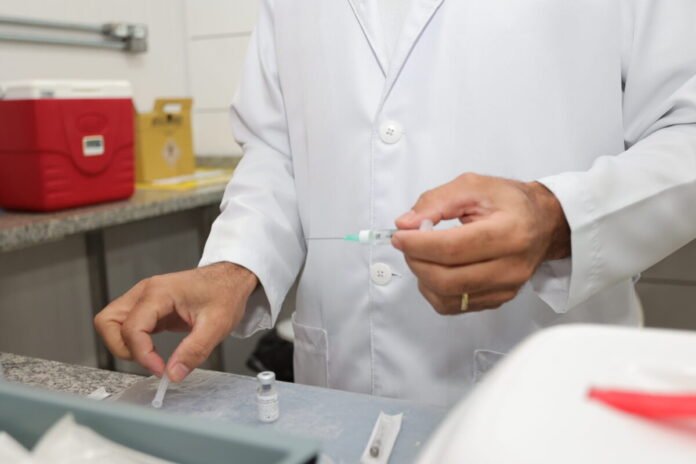 Healthcare professional in a white lab coat filling a syringe with vaccine at a clinical counter.
