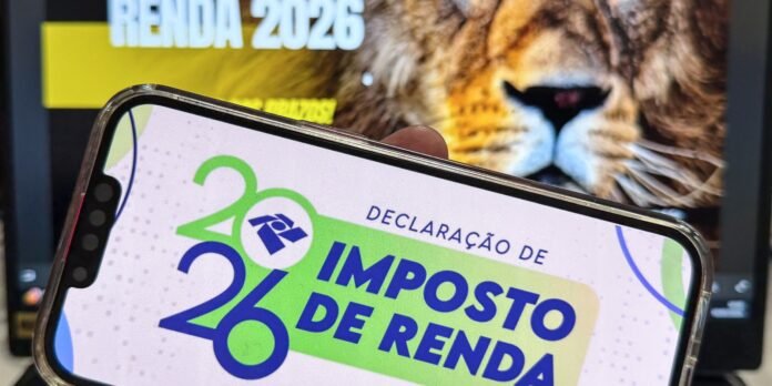 Smartphone screen showing a Brazilian tax return app reading 'Declaração de Imposto de Renda 2026' with a blurred tiger poster in the background.