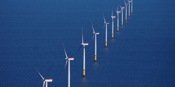Row of offshore wind turbines standing in calm blue sea, receding into the distance.