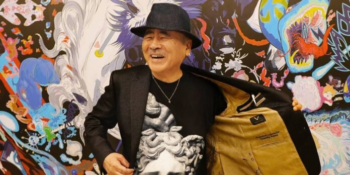 Smiling older man in a black blazer and hat opens his jacket to show the tan lining, with a vibrant graffiti mural in the background.