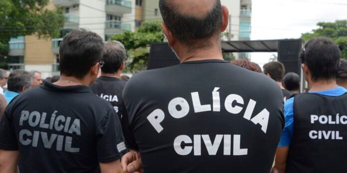 Backs of several people wearing black shirts with 'POLÍCIA CIVIL' in white letters, gathered at an outdoor event.