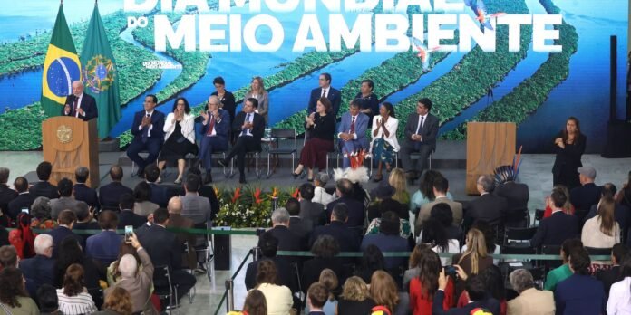 Speakers on a Brazilian stage with flags; seated panel, sign language interpreter, and an attentive audience against an environmental-themed backdrop.
