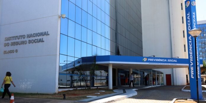 Exterior view of a modern government building with blue glass, sign reading Instituto Nacional do Seguro Social (INSS) and Previdência Social entrance.