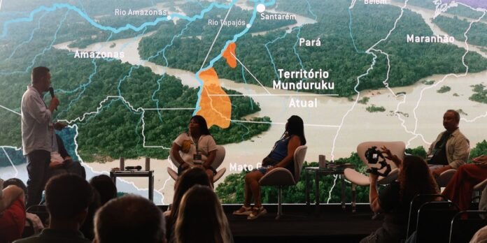 Panel discussion on a stage with four speakers and a large map backdrop showing Amazonas region and Munduruku territory behind them.