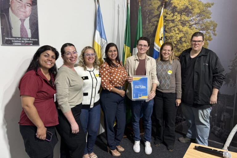 Seven people pose in an office; a man in the center holds a blue and yellow Cultura folder.