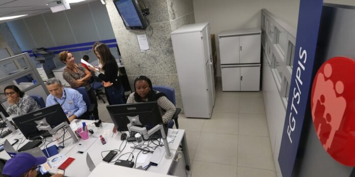 Open-plan service desk with four agents at desks and two women standing and discussing a document near the back, in a modern office.