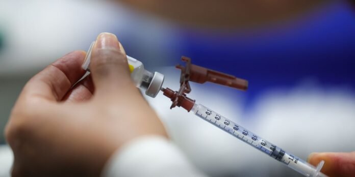 Close-up of hands drawing liquid into a syringe from a vial for vaccination or injection preparation.