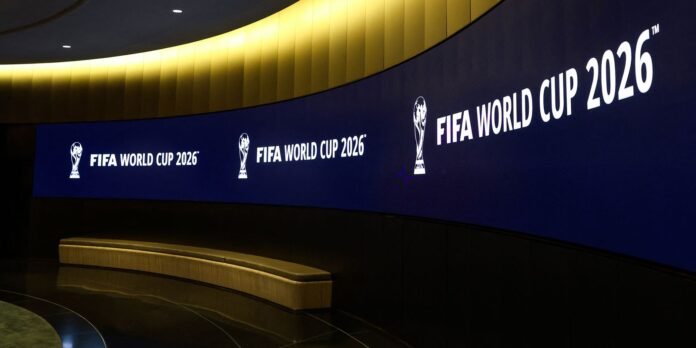 Curved blue wall display with 'FIFA WORLD CUP 2026' and trophy logos, a yellow curved ceiling, and a beige curved bench in a dim indoor space.