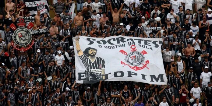 Large crowd of football fans in black-and-white striped jerseys waving a banner with 'ESTOPIM' and club crest in a stadium stands image by fans